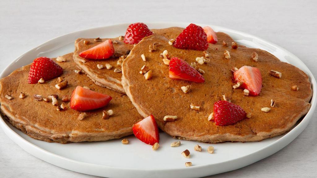 Fruit & Nut Multigrain Pancakes · Three multigrain pancakes with bananas and topped with fresh strawberries and pecan pieces.