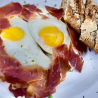 Huevos Rotos · Two sunny side up eggs served over a bed of homemade potatoes, sliced spanish serrano ham, m...