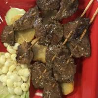 Anticuchos · Beef kabab at the grill served with sliced boiled potatoes and corn.