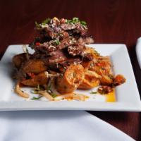 Pinchos De Res Asada · Grilled hanger steak on top of roasted potatoes with sautéed onions and chimichurri sauce.