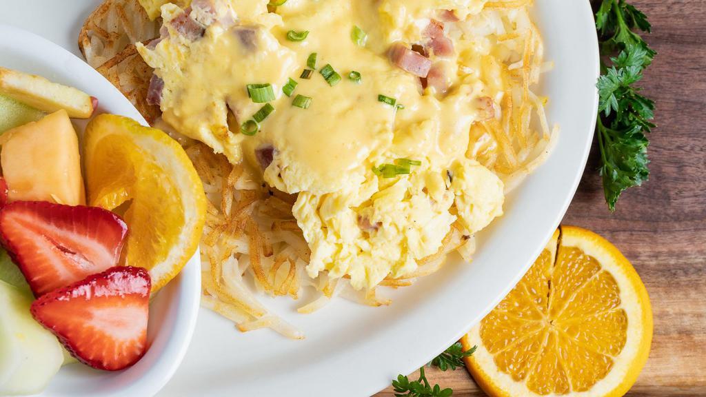 Country Benedict · Hash browns with grilled onions topped with scrambled eggs and country ham. Cover it with creamy hollandaise and a sprinkle of green onions. Served with a side of fruit and an English muffin.