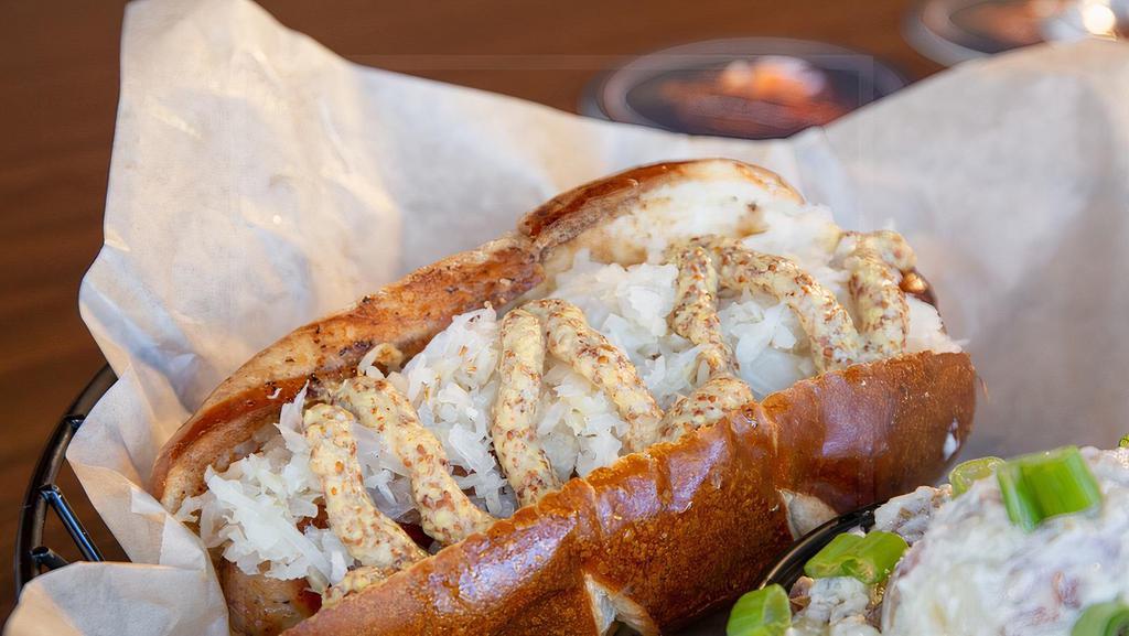 The German · 1/4 lb brat marinated in craft beer, served in a toasted pretzel bun with whole grain mustard and sauerkraut.