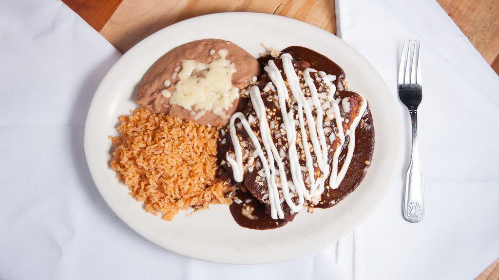 Enchiladas Con Mole (3) · Corn tortillas filled with shredded chicken dipped in mole sauce. (A very traditional sauce in mexico. Mix of chiles, chocolate and spices.) topped with Mexican cream, fresh cheese and onions. Served with Mexican rice and refried beans.