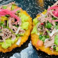 Tostada De Platano  · Plantain Tostada with shredded marinated beef with lime, guacamole, cilantro and red onions....