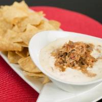 Shredded Pork Queso Dip · Warm white queso dip topped with seasoned shredded pork, served with tortilla chips