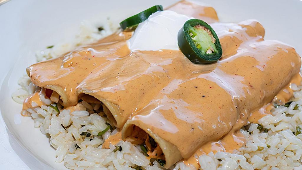 Southwest Seafood Enchiladas · Corn tortillas stuffed with Atlantic salmon, shrimp, wild Alaska Pollock, peppers, onions, and cheddar-jack cheese, topped with a light cream sauce, sour cream, and jalapeño. Served on a bed of cilantro lime rice.