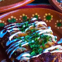 Black Mole Enchiladas · Black mole chicken enchiladas topped with queso and crema fresca. Comes with refried beans, ...