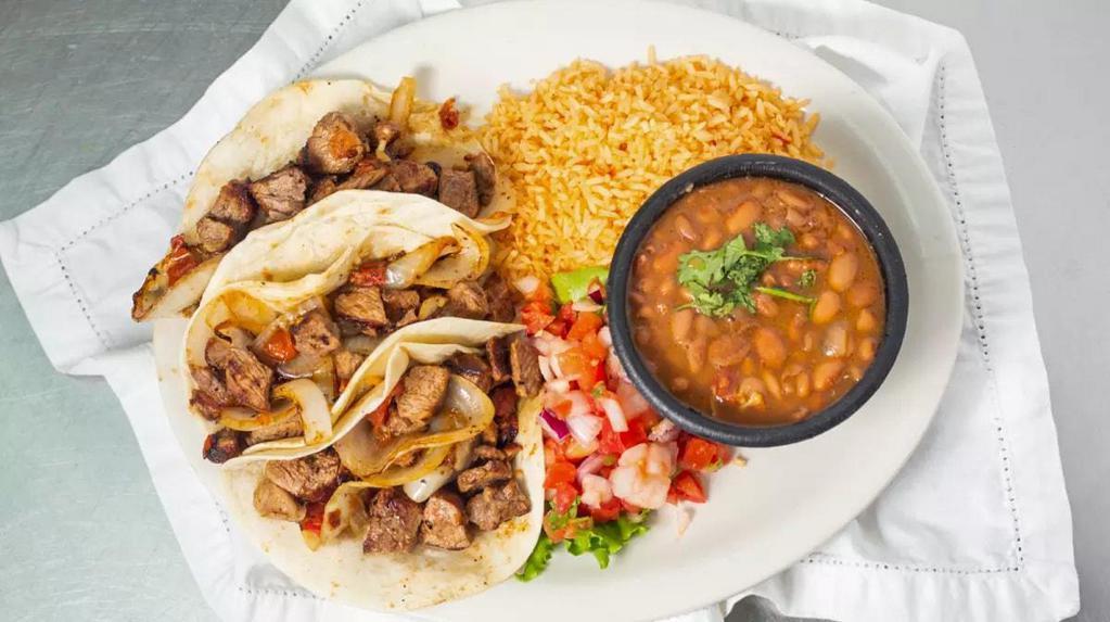 Tacos Al Carbon · Three flour tortillas filled with marinated, USDA Choice Angus sirloin steak, grilled onions and fresh tomatoes. Served with Mexican rice, charro beans and pico de gallo.