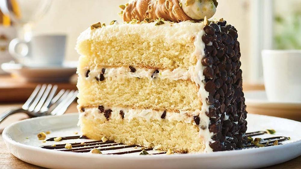 Cannoli Cake For Two** · Vanilla cake with layers of cannoli filling topped with a mini cannoli, pistachios and chocolate with a chocolate chip crust