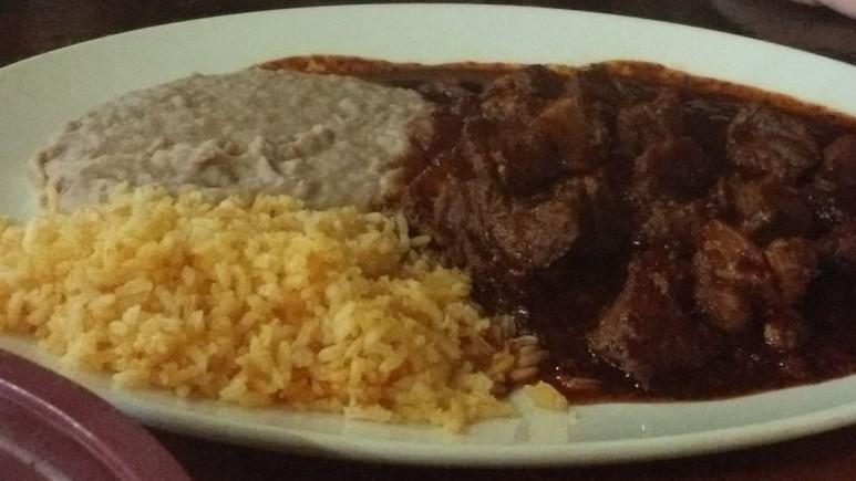 Asado De Puerco · Diced pork slowly cooked in red adobo pepper sauce served with Spanish rice and refried beans.
