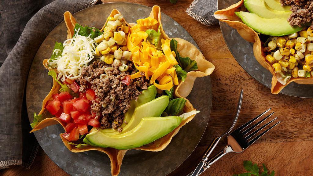 Taco Salad · A large crispy tortilla bowl filled  with fresh mixed greens topped with seasoned  chicken or beef, cheddar and Monterey Jack cheese, diced tomatoes, roasted corn medley. and sliced avocado. Add proteins for an additional charge.