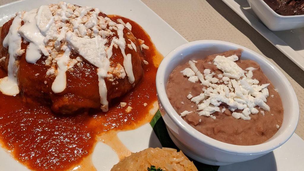 Chile Relleno · Roasted poblano pepper filled with your choice of ground beef, shredded chicken or cheese on a bed of red sauce, served with rice & beans.