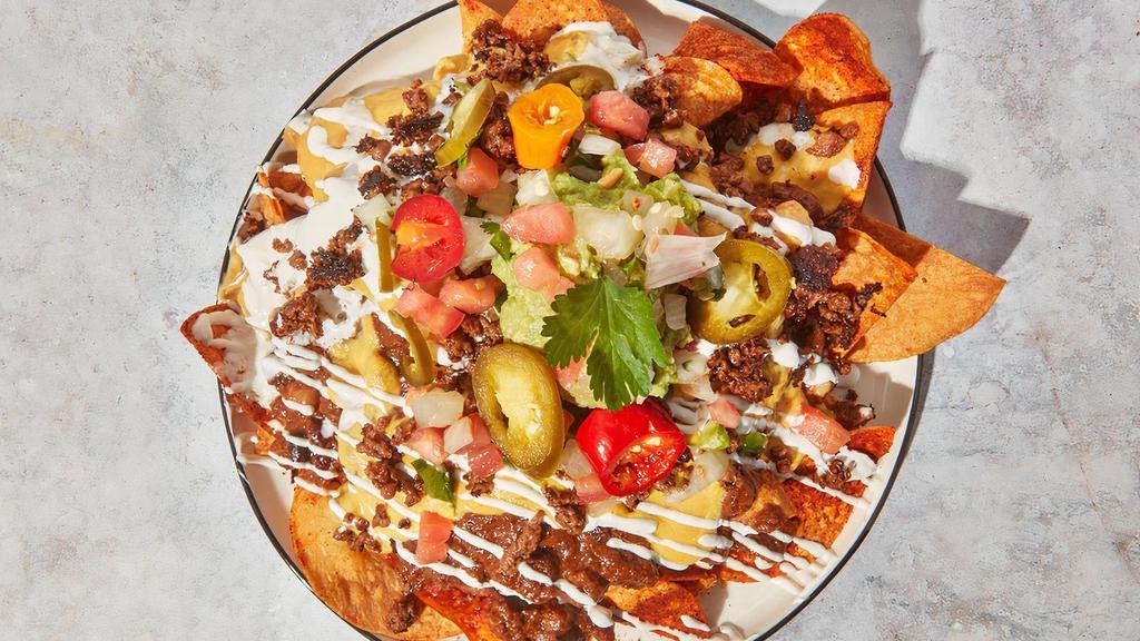 Deconstructed Nacho World · By TLC Vegan Kitchen. Fresh corn chips w/ house made chili, house made queso, Impossible crumble, vegan sour cream, pico de gallo, jalapenos, and avocado mash. Vegan and gluten-free. Contains soy, nightshades, and coconut. We cannot make substitutions.