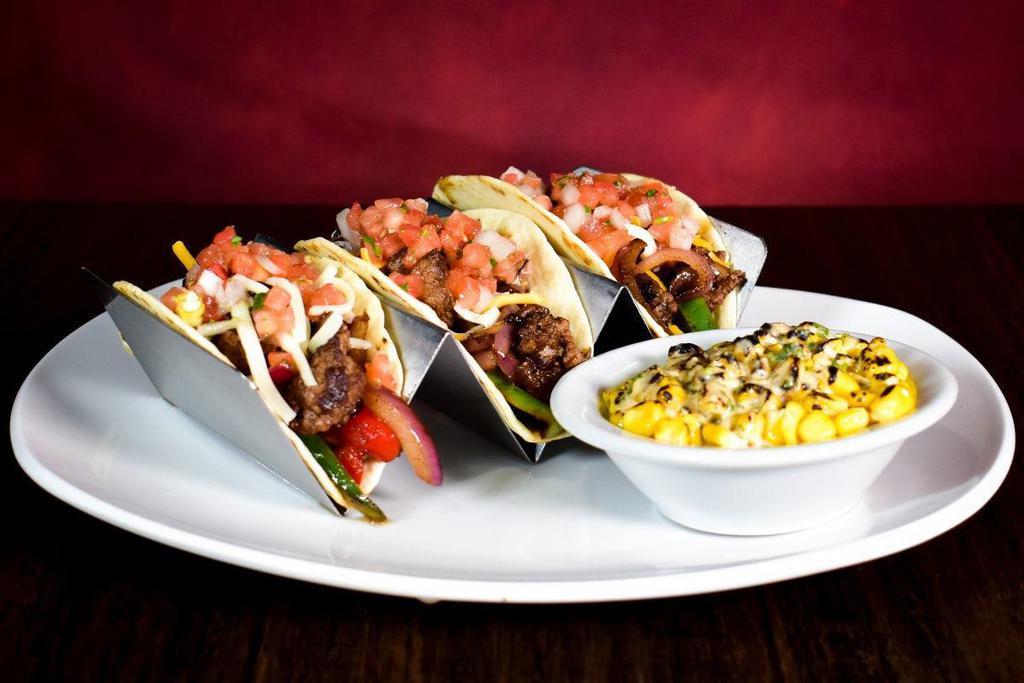 Steak Fajita Tacos · Tender marinated strips of steak, grilled onions, peppers, pico de gallo, cheddar & jack cheese loaded into grilled flour tortillas. Served with a side of off-the-cob elotes.