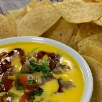 Texas Queso · Chile con queso topped with chopped brisket and pico de gallo. Fresh fried tortilla chips.