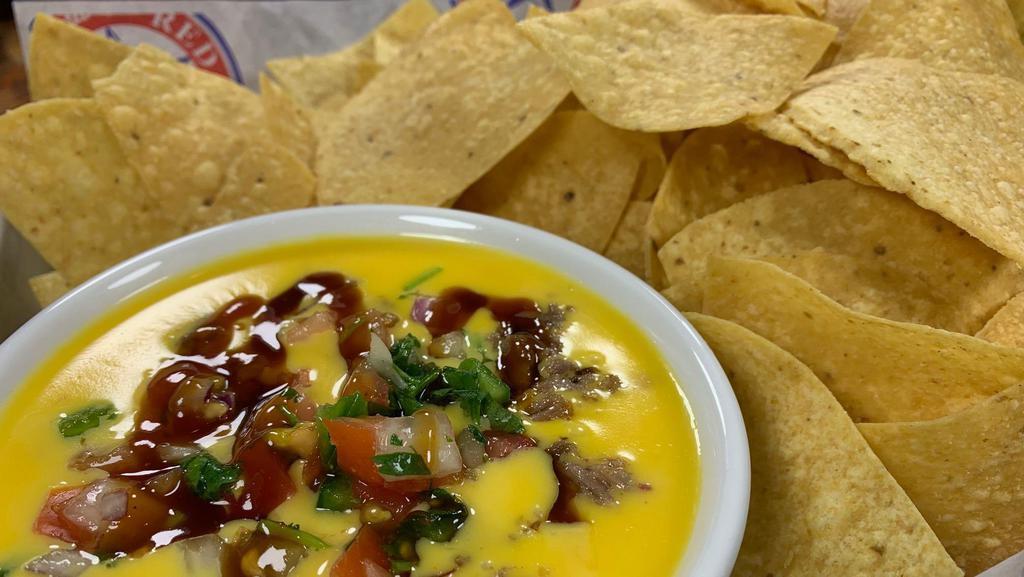 Texas Queso · Chile con queso topped with chopped brisket and pico de gallo. Fresh fried tortilla chips.