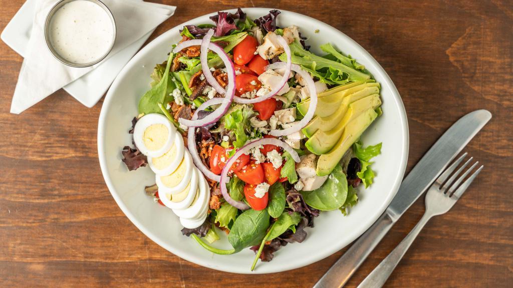 Cobb · Romaine lettuce topped with diced chicken, bacon, cherry tomatoes, red onion, blue cheese crumbles, hard boiled eggs, avocado, and side of a blue cheese dressing.