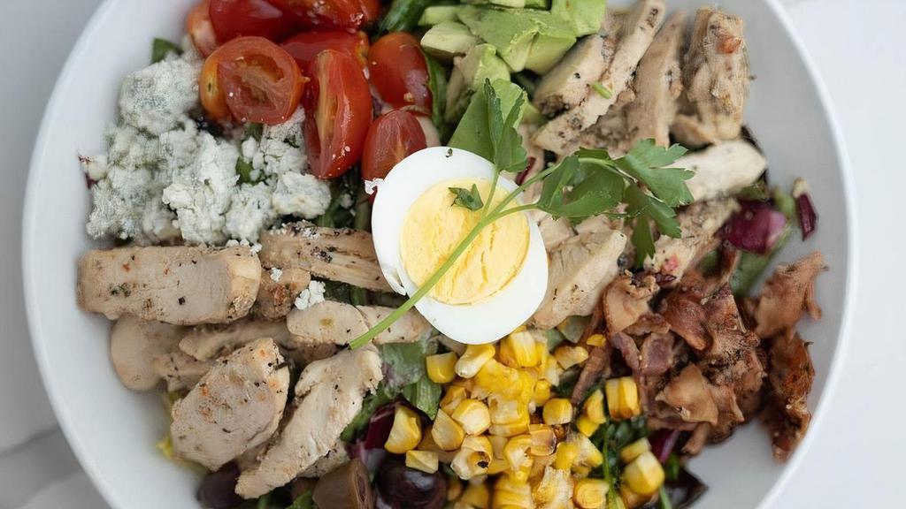 Cobb Salad · Roasted chicken, chopped pepper bacon, Gorgonzola cheese crumbles, cherry tomatoes, sliced Kalamata olives, roasted corn and diced avocado served on Spring mix, arugula and radicchio mix. Served with Blue Cheese Vinaigrette.