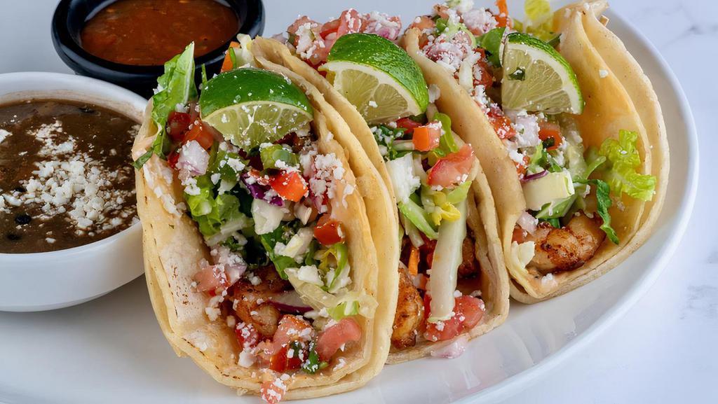 Baja Fish Tacos - Shrimp · Double stacked warm corn tortillas spread with chipotle aioli and layered with seasoned shrimp, Napa slaw tossed in Honey Lime Vinaigrette, pico de gallo and cotija cheese. Served with a side of Santa Fe black beans and a side of roasted Tomatillo salsa.