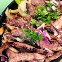 Tiger Cried · Grilled rib eye steak served over green onions, yellow onions, and mushrooms on a hot plate ...