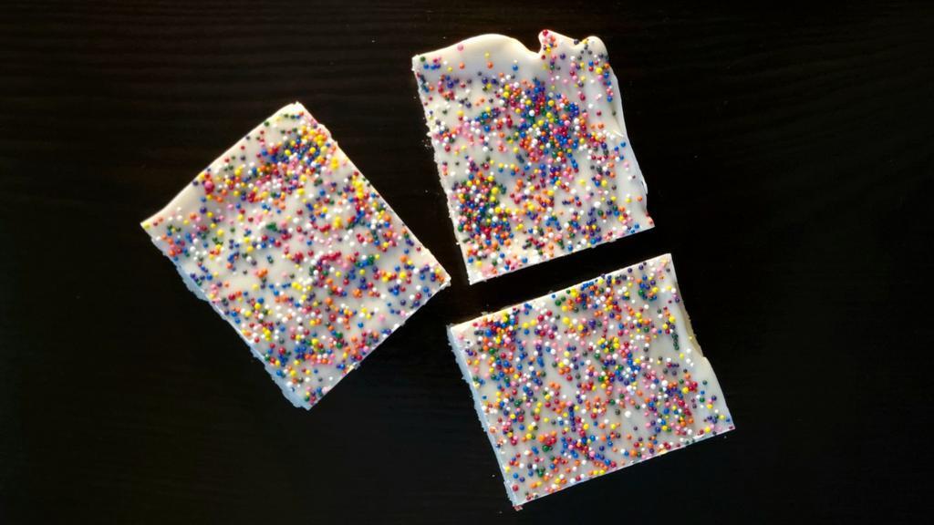 The Sprinkles · A bar with layers of shortbread, scrumptious white chocolate fudge, and white chocolate dotted generously with rainbow confetti sprinkles.
