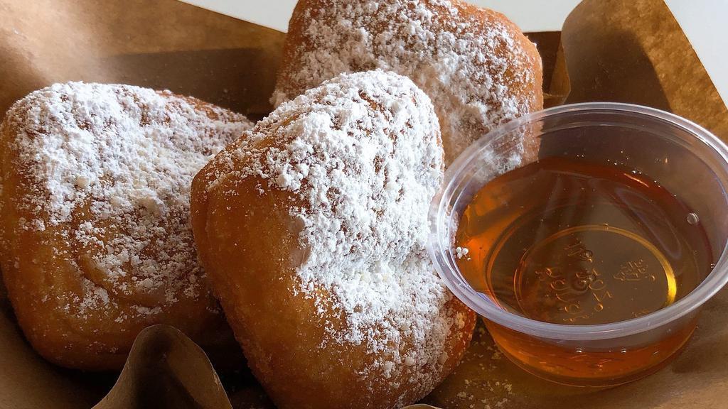 Beignets · Soft and fluffy squared shaped pastry. Lightly sprinkled with powdered sugar, served with honey.