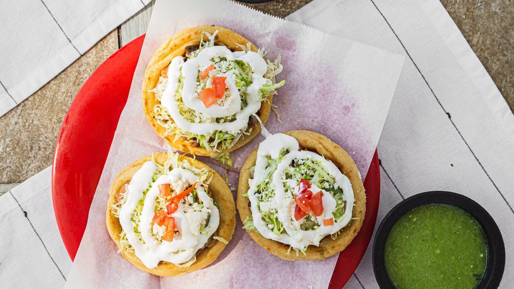Sopes · Three deep fried corn sopes topped with beans, meat of your choice, lettuce, Mexican sour cream, and sliced tomatoes/ Three sopes con fruoles, la carne de Su preferencia, lechuga, crema Mexicana, y tomates.