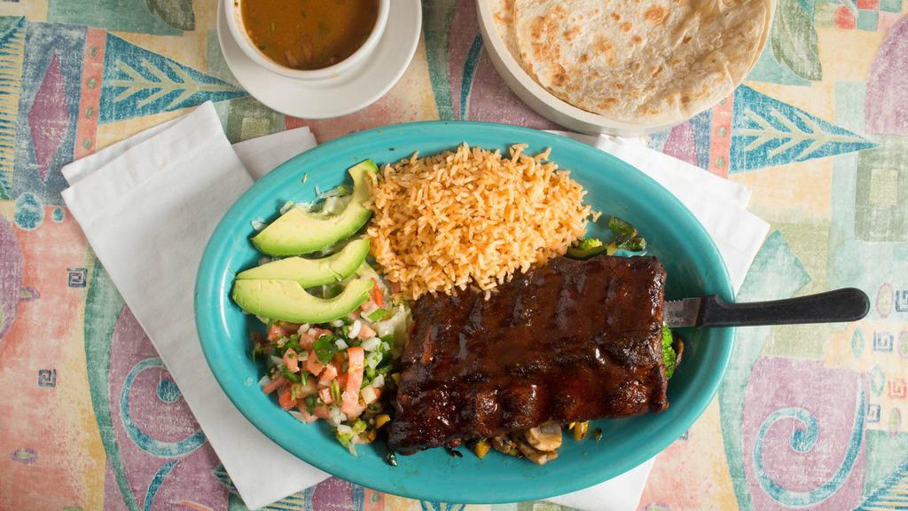 Costillas De Puerco · Pork ribs grilled to perfection topped with barbecue sauce served with rice, charro beans, guacamole and tortillas.