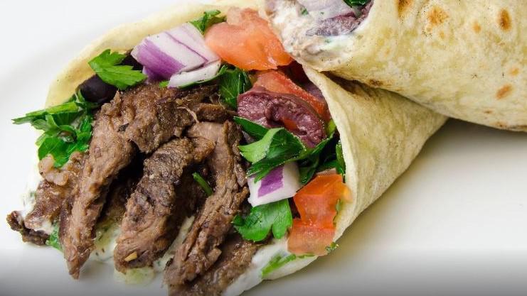 Beef Shawarma Wrap · Marinated beef thin sliced on pita bread with salad, lettuce, tomato, cucumbers, red onion, pickles, tzatziki sauce, and hot sauce, and tahini.