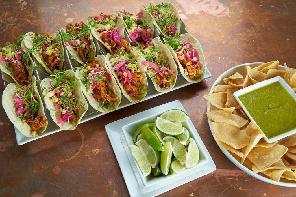 Chicken Tinga Tacos · House-smoked SPICY pulled chicken, avocado mash, pickled red onion, grilled corn, micro cilantro, queso fresco, white corn tortillas.. 12 tacos with chips and jalapeno salsa verde.. Add guacamole for $10.. Carry out only. Serves 4-6.