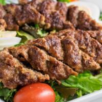 Beef Skewer Kebab Salad · A ground beef skewer kebab served on a plate of salad with dressing and cheese.