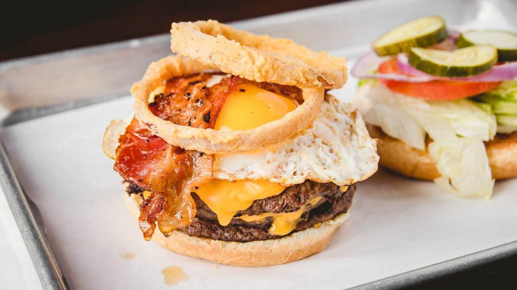 Hangover Burger · Two lean flame grilled patties, Swiss cheese, American cheese, bacon, fried onion rings, topped with a perfectly cooked egg.
