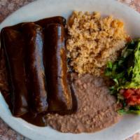Enchiladas In Mole · Three chicken enchiladas topped with mole poblano sauce. Served with Spanish rice, refried b...