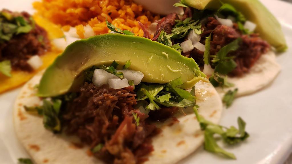 Barbacoa Tacos · Three braised lean beef cheek with corn tortillas. Served with cilantro, onions, avocado, rice and charro beans.
