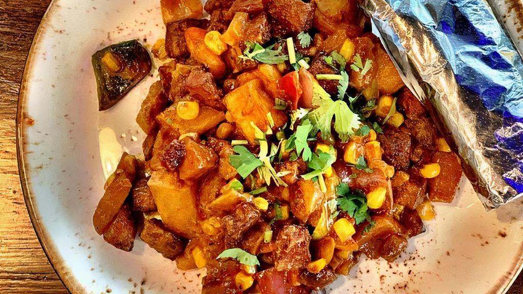 Revuelto Vegano · Vegan hash with sweet potatoes, plantains, potatoes, sweet corn, red bell pepper, red Vidalia onions, poblanos and epazote cooked in a guajillo-coconut sauce. Served with two corn tortillas