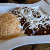 Enchiladas En Mole · Three chicken enchiladas topped with mole sauce, garnished with sesame seeds, queso fresco, ...