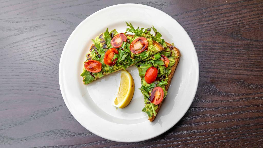 Avocado Toast · An avocado toast on multigrain bread. Topped with arugula, sliced cherry tomatoes, balsamic glaze, and served with a lemon slice.