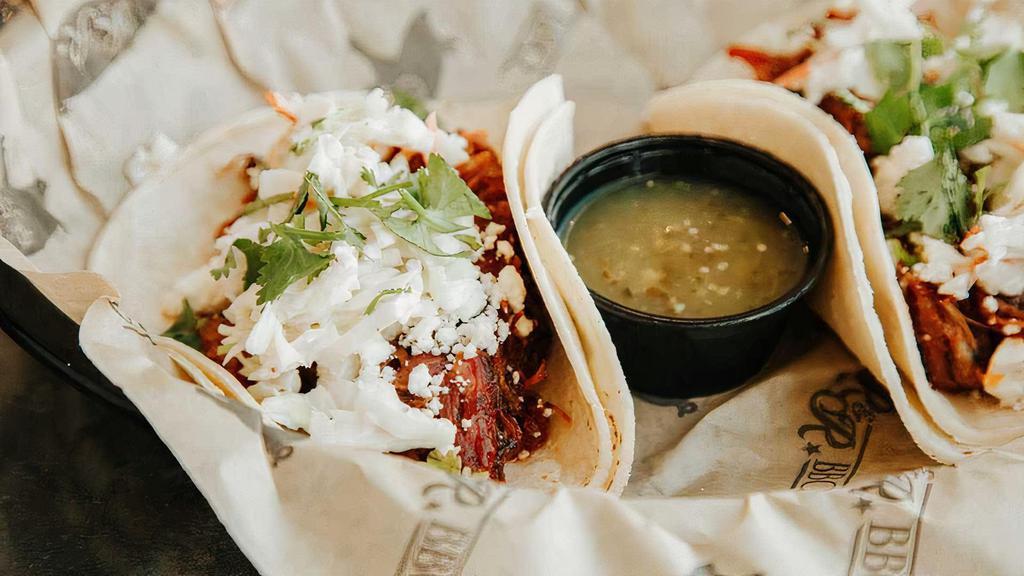 Bbq Pork Tacos · Pulled pork simmered in sweet BBQ sauce served on soft corn tortillas with coleslaw, cilantro, feta cheese, and tomatillo salsa.