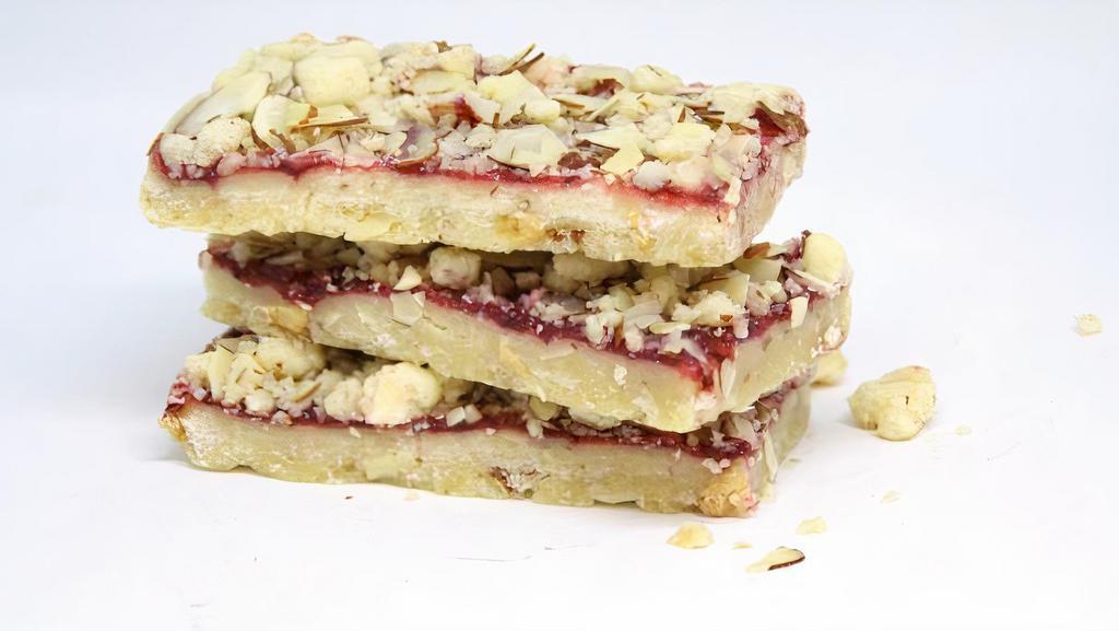 Rasberry Jammer Bar · Take a white chocolate shortbread base with crunchy almonds, add pure raspberry preserves and top with an almond shortbread crumble. This dessert bar is the perfect flavorful combination!