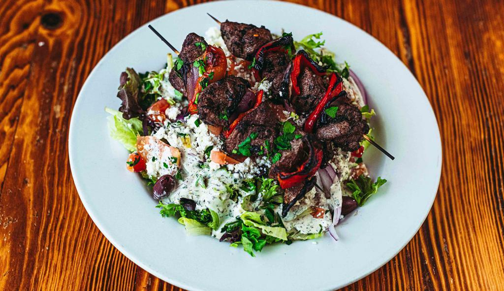 Lamb Kabob Salad · Lamb marinated in olive oil, garlic, mint, and lemon. Served with two skewers over mixed greens, cucumbers, tomatoes, onions, feta cheese, and kalamata olives then topped with our house dressing. GF