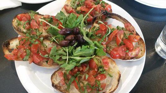 Bruschetta · Sliced bread topped with cherry tomatoes, basil, oregano, olive oil, served with arugula and olives.