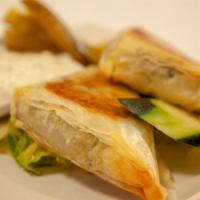 Spanakopita · Spinach and feta cheese wrapped in filo dough and baked. Served with Tzatziki sauce.