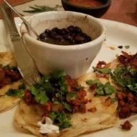 Street Tacos Al Pastor · Three pork soft tacos topped with cilantro and onion.