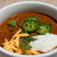 Vegan Chili · A generous portion of vegan chili topped with shredded vegan cheese and jalapeno slices.
