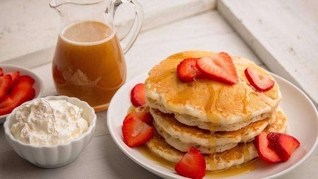 Homemade Sourdough Pancakes · 3 fluffy pancakes served with strawberries, whip cream and homemade caramel syrup.