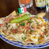 Nachos Chingones · Homemade corn tortilla chips layered with tender pork green chile, melted Oaxaca cheese, roa...