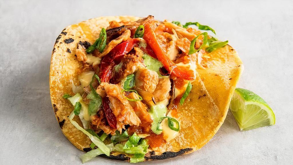 Chick'N Tinga Taco · Shredded chick'n, grilled onions, red bell peppers in a spicy roja sauce, topped with shredded lettuce, pico, queso sauce, green onions, and baja sauce and a lime wedge. Gluten-friendly. | 300 cals.