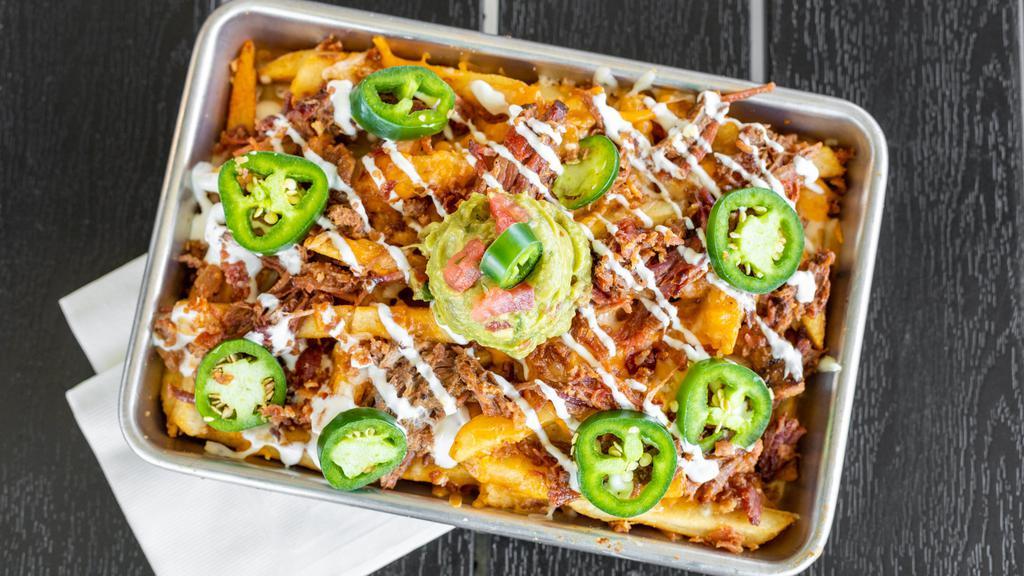 Smothered Brisket Fries · Topped with beef brisket, applewood bacon, cheddar jack cheese and Voodoo Ranger Queso, lime sour cream and jalapeños. Served with guacamole