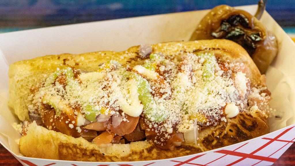 Estilo Sonora · Bun, bacon-rolled dog, topped with pinto beans, grilled onions, tomatoes, mayonnaise, mustard, ketchup, guacamole, jalapeño, salsa and Parmesan cheese.