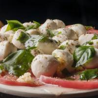 Caprese Salad · Fresh mozzarella layered with sliced tomatoes and topped with herbs.